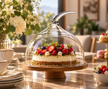 Lade das Bild in den Galerie-Viewer, OONYQ Crystal Cake Cover Ø 308 mm – bruchsichere Tortenhaube aus Tritan mit geschwungenem Griff über Cheesecake auf Holz-Tortenständer