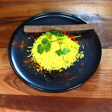 Lade das Bild in den Galerie-Viewer, Schwarzer Keramik-Speiseteller Goma Ø 25 cm mit gelbem Reis, Zimtstange und Koriander, serviert auf Holztisch